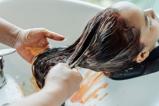 Fryzjer spłukuje mieszankę z włosów kobiety po dekoloryzacji. Woda ma lekko pomarańczowy kolor.