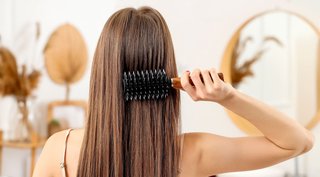 Młoda dziewczyna odwrócona plecami stylizuje włosy używając szczotki 