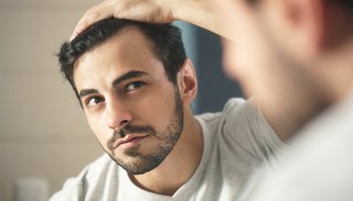 Mężczyzna przeczesujący włosy i oglądający pierwsze oznaki przerzedzania się włosów