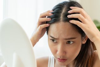 Młoda kobieta przed lustrem trzyma dłonie na głowie i patrzy na swoje włosy.