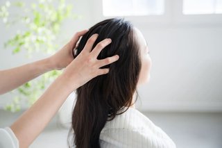 Kobiece dłonie masują skórę głowy drugiej kobiecie z długimi włosami