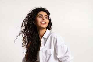 Młoda kobieta z ciemnymi, kręconymi lokami w białej koszuli