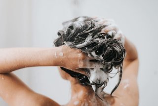 Młoda kobieta myje tłuste włosy u nasady szamponem
