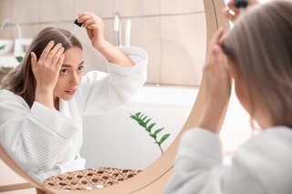 Kobieta przed lustrem w szlafroku aplikuje serum na skórę głowy
