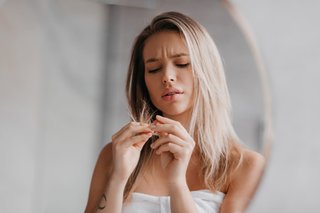 Młoda kobieta o blond włosach przyglądająca się suchym końcówkom